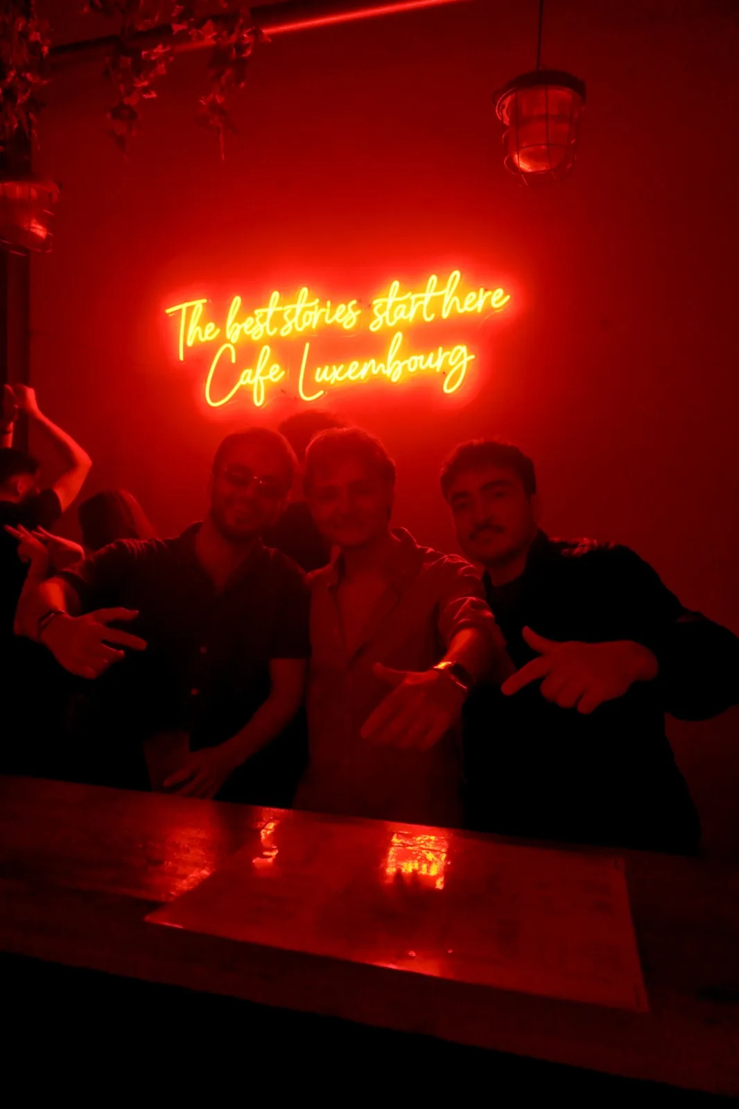Three guests posing under the Café Luxembourg neon sign